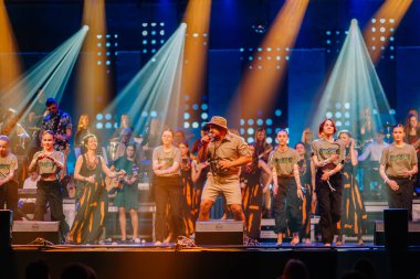 Valmiera, Letonya - 29 Aralık 2025: Yamaha. Erkek vokalist, canlı bir atmosferde enerjik dans grubu ve dinamik ışıklandırma ile sahnede seyirciyi cezbediyor.