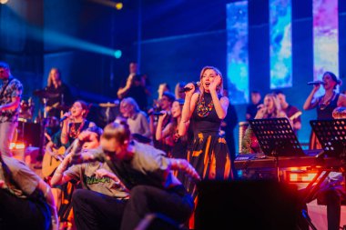 Valmiera, Letonya - 29 Aralık 2025: Yamaha. Şarkıcı, müzisyenler ve renkli ışıklarla çevrili sahnedeki güçlü performansıyla seyirciyi büyülüyor.