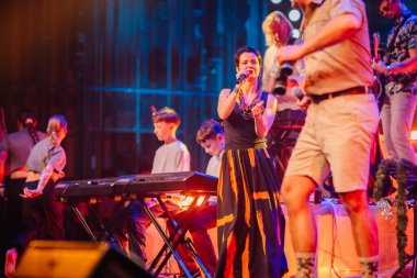 Valmiera, Letonya - 29 Aralık 2025: Yamaha. Şarkıcı, enerjiyle dolu canlı konser ortamında enstrüman çalan müzisyenlerle sahnede seyircileri büyülüyor.