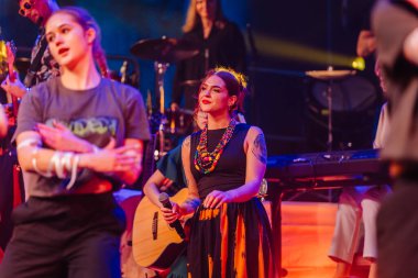 Valmiera, Letonya - 29 Aralık 2025: Yamaha. Kadın şarkıcı, canlı müzik performansı sırasında renkli kıyafetler ve canlı ışıklandırmayla sahnede seyirciyi büyülüyor.