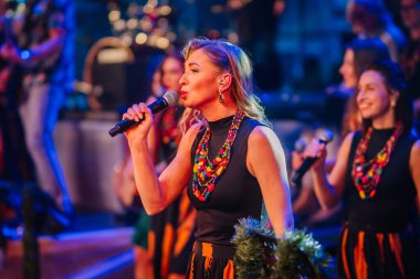 Valmiera, Letonya - 29 Aralık 2025: Yamaha. Kadın vokalist sahnede tutkuyla şarkı söylüyor. Renkli kıyafetler ve parlak ışıklarla enerjik bir atmosfer yaratıyor.