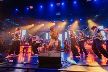 Valmiera, Letonya - 29 Aralık 2025: Yamaha. Erkek dansçı, renkli ışıklar ve cazip bir atmosfer yaratan müzisyenlerle sahnede dinamik hareketler sergiliyor