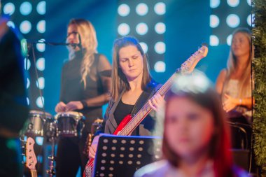 Valmiera, Letonya - 29 Aralık 2025: Yamaha. Sahnede elektro gitar çalan bir kadın. Renkli ışıklar ve diğer müzisyenler arka planda sahne alıyor.