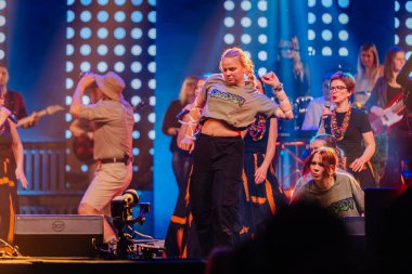 Valmiera, Letonya - 29 Aralık 2025: Yamaha. İki genç kadın renkli ışıklar ve coşkulu kalabalıkla dolu canlı bir müzik festivalinde sahnede enerjik bir şekilde dans ediyorlar.