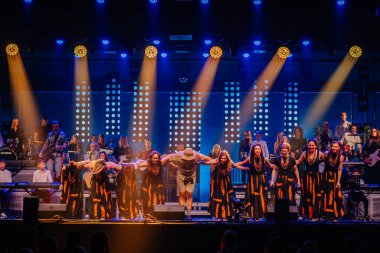 Valmiera, Letonya - 29 Aralık 2025: Yamaha. Parlak ışıklar ve enstrümanlarla dolu enerjik bir müzikal performansın ardından geleneksel giyinmiş sanatçılar sahnede selamlıyorlar.