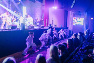 Valmiera, Letonya - 29 Aralık 2025: Yamaha. Beyaz elbiseli birden fazla dansçı renkli ışıklar altında sahnede enerjik bir performans sergiliyor.