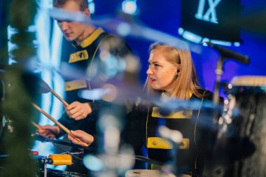 Valmiera, Letonya - 29 Aralık 2025: Yamaha. Kadın davulcu, canlı performans sırasında siyah ve sarı üniformalı erkek müzisyenle birlikte sahnede çalıyor.