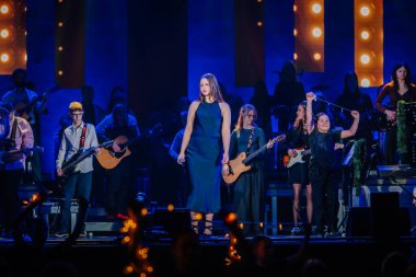 Valmiera, Letonya - 29 Aralık 2025: Yamaha. Şarkıcı, canlı bir konser ortamında enstrüman çalan müzisyenlerle sahnede seyircileri büyülüyor.