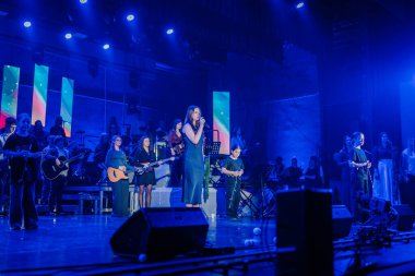 Valmiera, Letonya - 29 Aralık 2025: Yamaha. Şarkıcı, renkli ışıklarla dolu canlı konser atmosferindeki müzisyenlerle sahnede seyircileri cezbediyor.