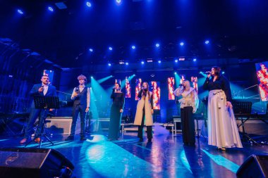 Valmiera, Letonya - 29 Aralık 2025: Yamaha. Canlı bir konser sırasında altı vokalist renkli ışıklar ve canlı bir atmosferle sahnede performans sergiliyor.