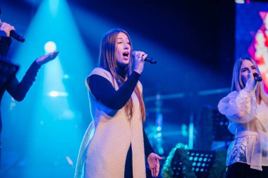 Valmiera, Letonya - 29 Aralık 2025: Yamaha. Sahnede, mavi ışıklarla çevrili, enerjik bir atmosfer yaratan kadın vokalist.