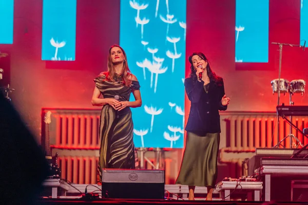 Valmiera, Letonya - 29 Aralık 2025: Yamaha. Kadın vokalistler, bir konser sırasında renkli ışıklandırma ve çiçek arkaplanıyla sahnedeki seyircileri büyülüyor.