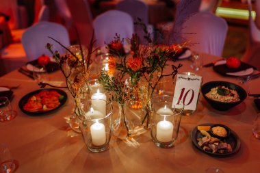 Şenlikli yemek masası mumlar, çiçekler ve tabaklar ile güzelce düzenlenir, kutlamalar ve toplantılar için davetkar bir ortam yaratır, özel durumlar için mükemmeldir.