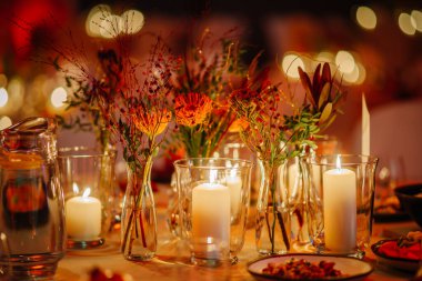 Cam vazolarda mumların ve renkli çiçeklerin bulunduğu güzel bir masa, özel bir etkinlik ya da kutlama için davetkar atmosferi arttırır.