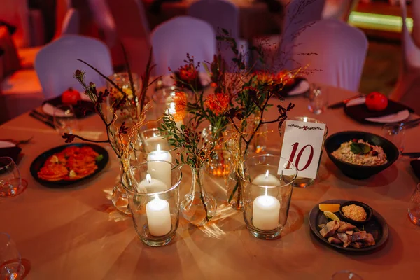 Şenlikli yemek masası mumlar, çiçekler ve tabaklar ile güzelce düzenlenir, kutlamalar ve toplantılar için davetkar bir ortam yaratır, özel durumlar için mükemmeldir.