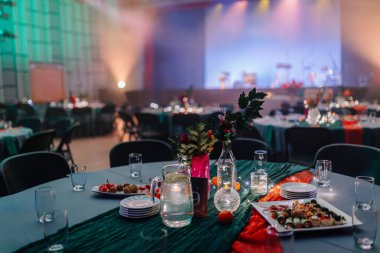 Renkli masa örtüleri, çiçekli süslemeler ve ortam aydınlatmalı zarif masaların yer aldığı şölen sahnesi, kutlama için canlı bir atmosfer yaratıyor.