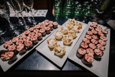 Zarif tatlı tabakları beyaz tabaklar üzerinde çeşitli renkli mini pastalar ve tatlı ikramlar sunar. Bayram kutlamaları ve özel günler için idealdir.