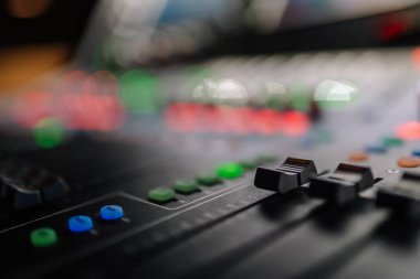 Canlı düğmeler ve kaydıraklardan oluşan bir ses karıştırma konsolunun ayrıntılı yakın çekimi, ses mühendisliği ve müzik üretim süreçlerinin karmaşıklığını vurguluyor