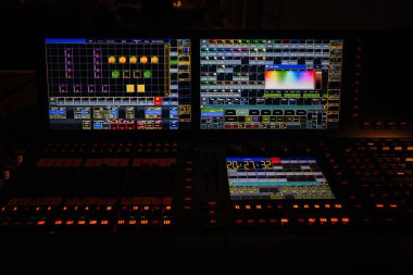 Yüksek teknoloji ses karıştırma konsolu aydınlatma kontrolleri ve canlı ekranlar, modern bir stüdyo ortamında karmaşık ses mühendisliği ve üretim kapasitesi göstermektedir.