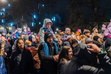 Valmiera, Letonya - 30 Kasım 2025: Omuzlarında çocuklar ve sahneyi aydınlatan parlak ışıklarla bir gece etkinliğini kutlayan insanların canlı bir araya gelmesi
