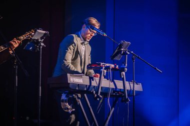 Sigulda, Letonya - 05 Aralık 2025: Şirket galası. Müzisyen sahnede mavi ışıklandırmalı Yamaha klavyesi çalıyor, canlı performans sırasında enerjik bir atmosfer yaratıyor.