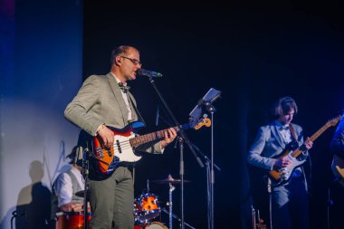 Sigulda, Letonya - 05 Aralık 2025: Şirket galası. Sahnede bas gitar çalan erkek müzisyen sahne ışıkları altında arka planda konser veriyor.