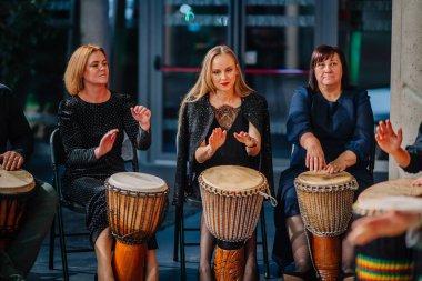 Sigulda, Letonya - 05 Aralık 2025: Şirket galası. Canlı bir ortamda ritmik davul çalan, kültürel ifade sergileyen ve enerjik enerji veren üç kadın.