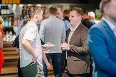 Sigulda, Letonya - 05 Aralık 2025: Şirket galası. Erkekler bir ağ etkinliğinde sosyalleşiyorlar, çağdaş bir ortamda içeceklerin ve aperatiflerin tadını çıkarıyorlar.