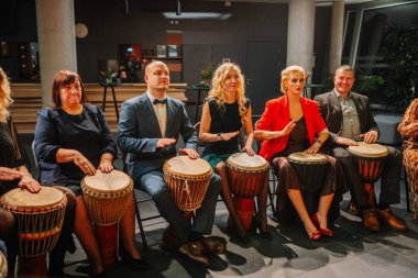 Sigulda, Letonya - 05 Aralık 2025: Şirket galası. Çeşitli yetişkin grupları canlı enerjili, kapalı bir ortamda davul çalıyorlar.