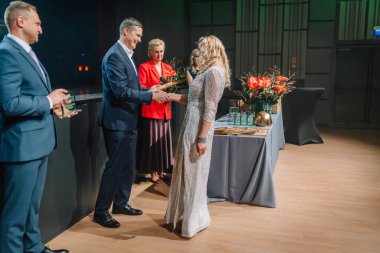 Sigulda, Letonya - 05 Aralık 2025: Şirket galası. Çiçek aranjmanları ve neşeli atmosferiyle seremoni sırasında çarpıcı elbiseli kadın ödüllendiriliyor.