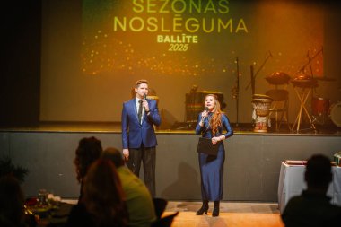 Sigulda, Letonya - 05 Aralık 2025: Şirket galası. Zarif kıyafetler içindeki sunucular canlı fon ve müzik enstrümanlarıyla sahnede bir etkinlik düzenliyorlar.