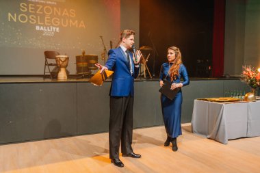 Sigulda, Letonya - 05 Aralık 2025: Şirket galası. Erkek sunucu ve kadın sunucu Sezonas Nosleguma etkinliğinde sahne dekorasyonlarıyla seyircilerle etkileşim halindeler