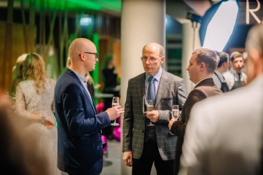 Sigulda, Letonya - 05 Aralık 2025: Şirket galası. Takım elbiseli bir grup adam, içkiler ve canlı bir atmosferle sofistike bir etkinlikte tartışıyorlar.