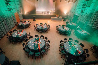 Sigulda, Letonya - 05 Aralık 2025: Şirket galası. Şölen salonu gösterileri, şenlikli bir atmosfer için canlı dekorasyonlar ve ortam aydınlatmalarıyla süslenmiş masaların etrafında.