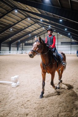 Riga, Letonya - 08 Kasım 2019: Kadın biniciler arenada kum tabanı ve parlak ışıklarla at biniyor