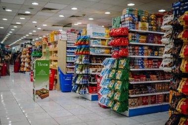 Dubai, Birleşik Arap Emirlikleri - 16 Ocak 2026: Renkli market koridorunda raflarda abur cuburlar, içecekler ve paketlenmiş mallar sergileniyor, parlak ışıklandırma görünürlüğü artırıyor