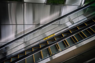 Yürüyen merdiven, çağdaş mimari tasarım yönlerini vurgulayarak çağdaş şehir ortamında sarı güvenlik işaretleri ve parlak metal yüzeylere sahiptir.