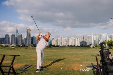Dubai, Birleşik Arap Emirlikleri - 17 Ocak 2026: Beyaz elbiseli son sınıf erkek golfçü Ufuk çizgisi görünen Dubai 'de atış talimi yapıyor