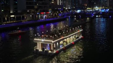 Dubai, Birleşik Arap Emirlikleri - 11 Ocak 2026: Aydınlatılmış yemek teknesi, gece Dubai limanında canlı şehir ışıklarıyla su üzerinde pırıl pırıl parlıyor.