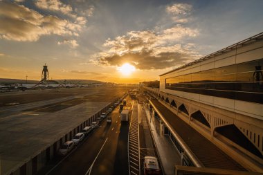 Dubai, Birleşik Arap Emirlikleri - 18 Ocak 2026: Dubai DBX havaalanında gün batımı Terminal binalar, pist ve bulutlu park edilmiş araçlar sergileniyor