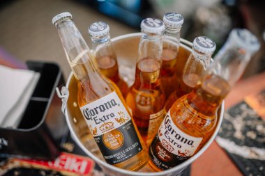 Riga, Letonya - 27 Eylül 2025: Corona Extra bira şişeleri ahşap bir masanın üzerinde bulanık bir bar arka planına sahip metal bir kovada düzenlenir