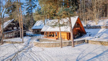 Kuldiga, Letonya - 30 Ocak 2026: Ağaçlı ve taş duvarlı karlı bir ortamda ahşap kulübe, arka planda ek kamaralar