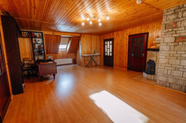 Kuldiga, Letonya - 30 Ocak 2026: Ahşap duvarlar ve tavandan oluşan rahat bir oda, kitap rafları olan bir masa ve sıcak bir atmosfer yaratan taş bir şömine