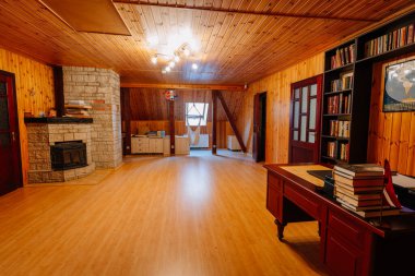 Kuldiga, Letonya - 30 Ocak 2026: Taş şöminesi, kitap rafları ve doğal ışığın içeri girmesine izin veren geniş pencereli ahşap oda