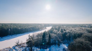 Kuldiga, Letonya - 30 Ocak 2026: Karla kaplı ağaçlarla çevrili donmuş bir nehrin havadan bakışı ve açık mavi gökyüzünde parlak bir güneş
