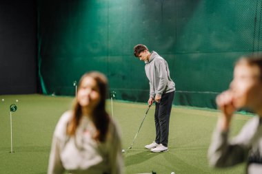 Genç adam, golf sahasında birkaç deliği olan yeşil bir yüzeye antrenman yapmaya odaklanıyor.