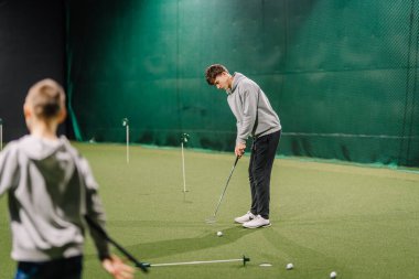 Erkek golfçü, golf eğitim tesisinde AİDS ve yeşil zemin ile birlikte kapalı alanlarda pratik yapmaya odaklanır.