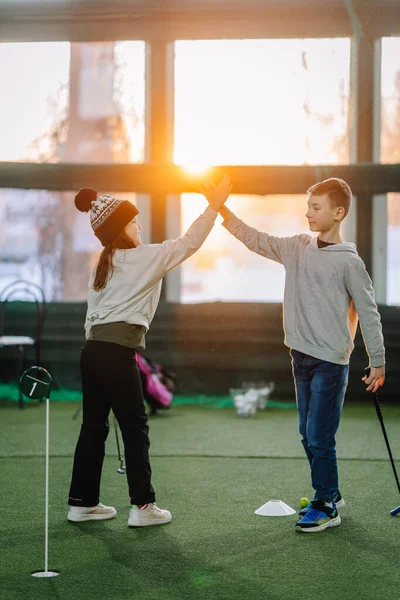 İki çocuk içeride golf oynarken arkadaşça bir beşlik çakıyor. Etrafı yapay çim ve büyük pencerelerle çevrili ve güneş ışığını içeri alıyor.