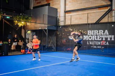 Riga, Letonya - 24 Ocak 2026: Padel turnuvası. İki adam mavi bir kortta, duvarları işaretli ve arka planda izleyen izleyicilerle Padel oynuyor.
