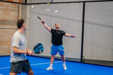 Riga, Letonya - 24 Ocak 2026: Padel turnuvası. Erkek Padel oyuncuları kapalı alanda maç yapıyor, bir oyuncu servis yaparken diğeri karşılık vermeye hazır.